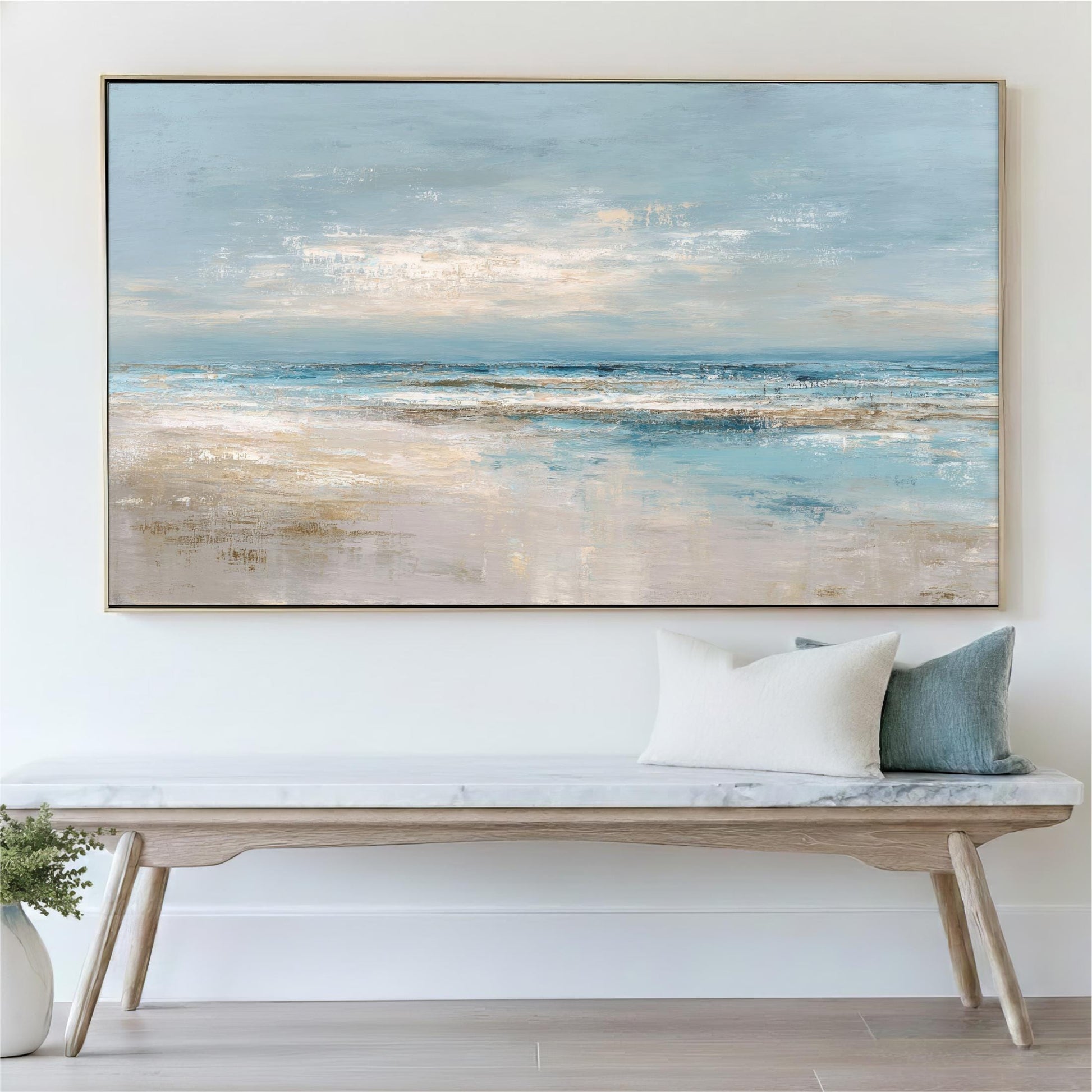 a large painting of a serene beach scene hanging on a wall above a wooden bench with a white cushion.