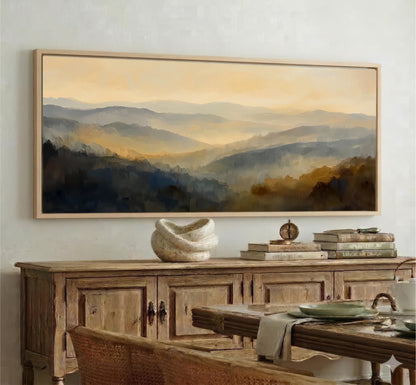 a large painting of a mountainous landscape hanging on a wall above a wooden cabinet. The cabinet has a vase and some books on top of it. In the foreground, there is a dining table with chairs and a bowl on it.