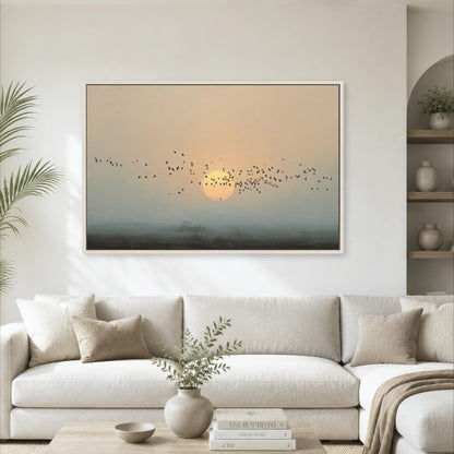 a large framed painting of a flock of birds flying over a landscape with a sunset in the background, hanging on a white wall above a white sofa in a living room setting.