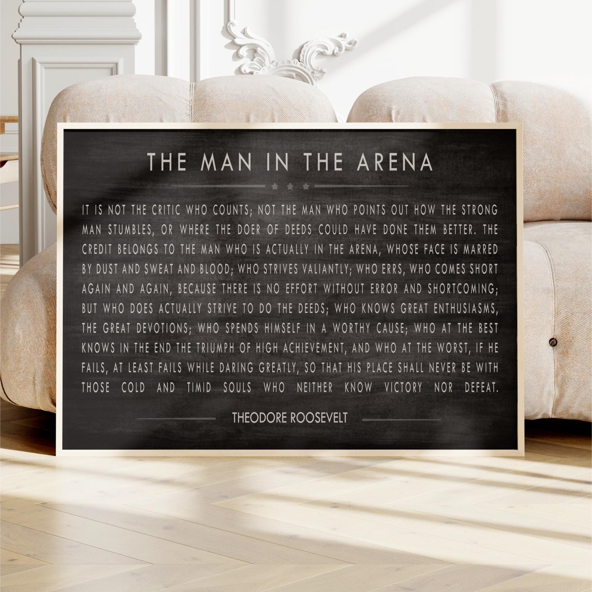 a framed quote by Theodore Roosevelt, a famous American president, placed on a wooden floor in front of a white sofa.