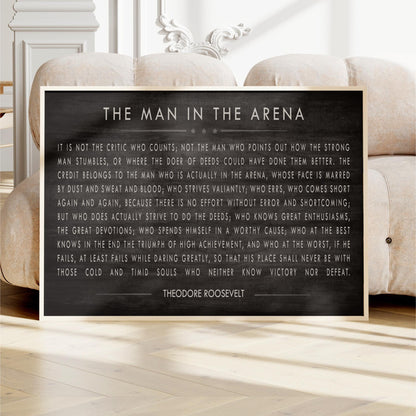 a framed quote by Theodore Roosevelt, a famous American president, placed on a wooden floor in front of a white sofa.
