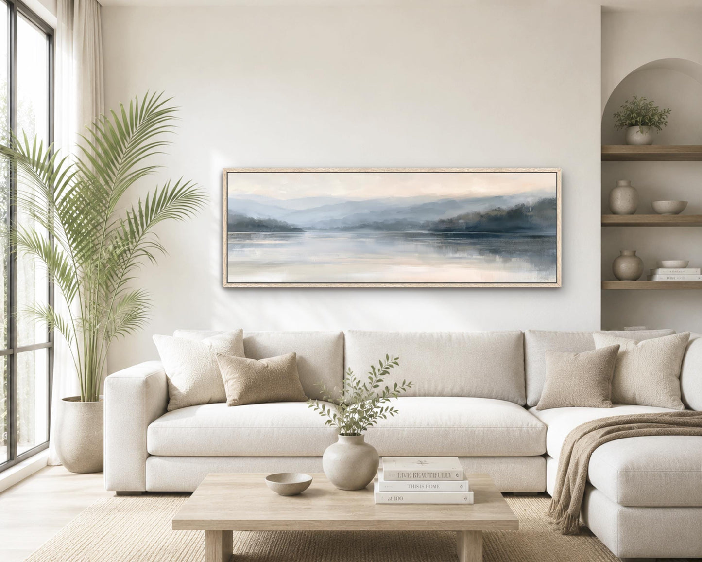 a serene living room with a large painting of a landscape hanging on the wall above a white sofa. The room is decorated with a potted plant, a vase with greenery, and a stack of books on the coffee table.