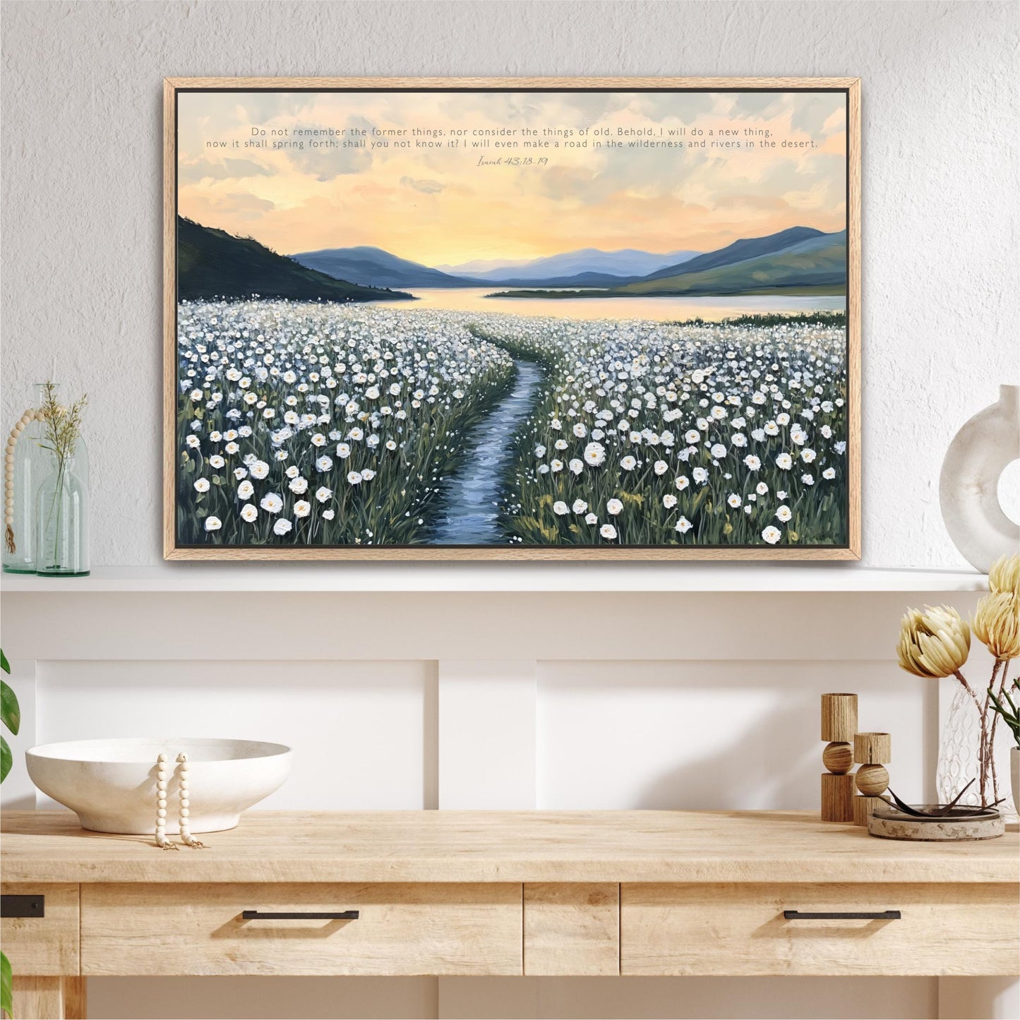 a large framed painting of a field of white flowers with a winding path leading through it, set against a backdrop of mountains and a sunset sky.