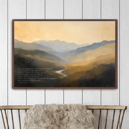 a framed painting of a mountainous landscape with a river winding through it, hanging on a white wall above a wooden bench.