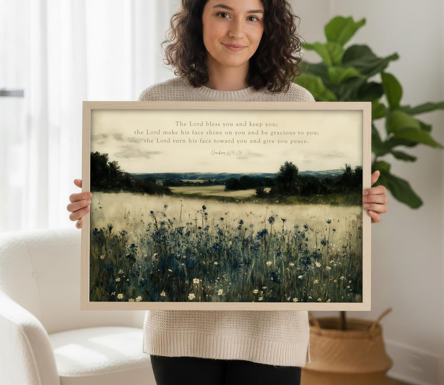 A woman is holding a framed print of a pastoral landscape with a field of flowers and trees.