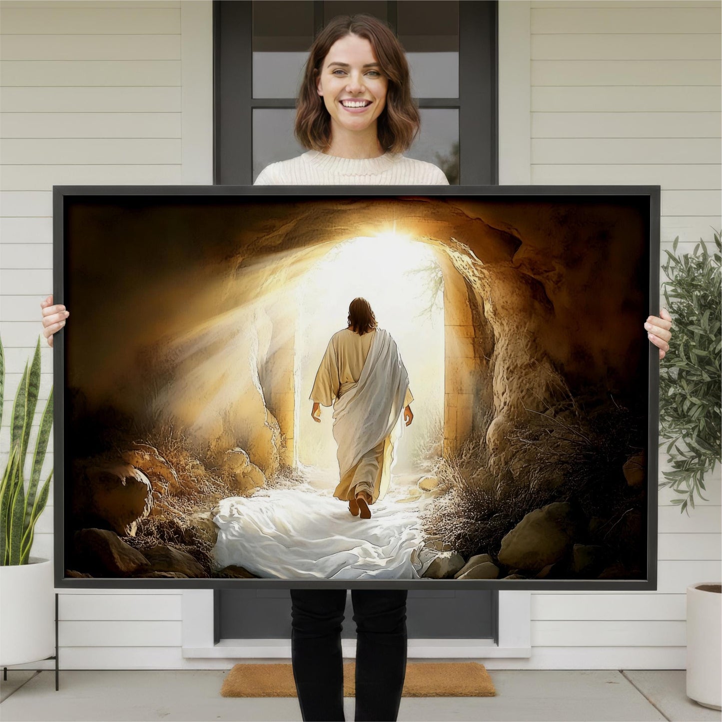 A woman is holding a large framed print of a painting depicting a man walking out of a cave or tunnel, with sunlight shining through the opening.
