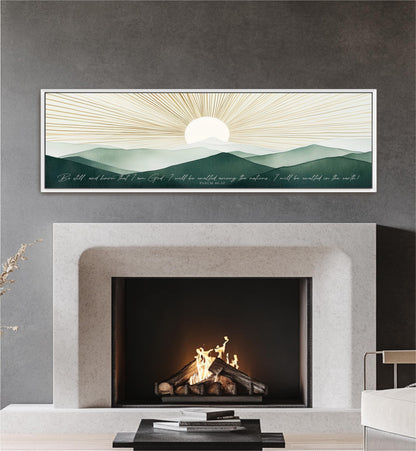 a fireplace with a warm fire burning inside, set against a backdrop of a serene landscape with mountains and a sun-like design. Above the fireplace, there is a framed artwork depicting a sunrise or sunset over a mountainous terrain. The artwork is framed in a white frame and hangs on a gray wall.