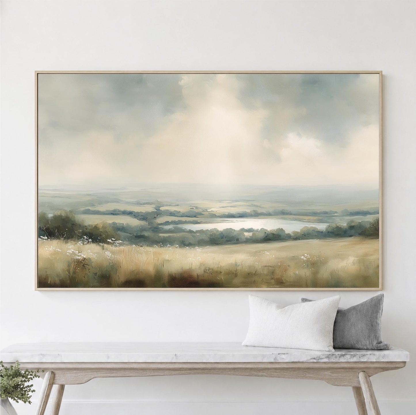a large landscape painting hanging on a white wall above a wooden bench with two pillows.
