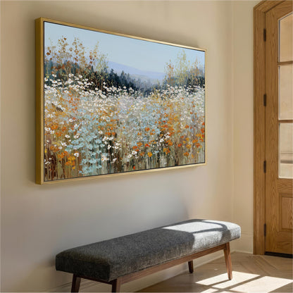 a large, framed painting of a field of flowers hanging on a wall. The painting is vibrant and colorful, depicting a serene landscape with a variety of flowers in different shades of white, orange, and yellow. The painting is positioned above a gray bench, which is placed in front of the wall. The overall scene creates a peaceful and inviting atmosphere in the room.