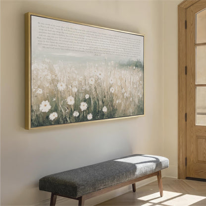 a large framed painting of a field of white flowers hanging on a wall, with a gray bench placed in front of it.