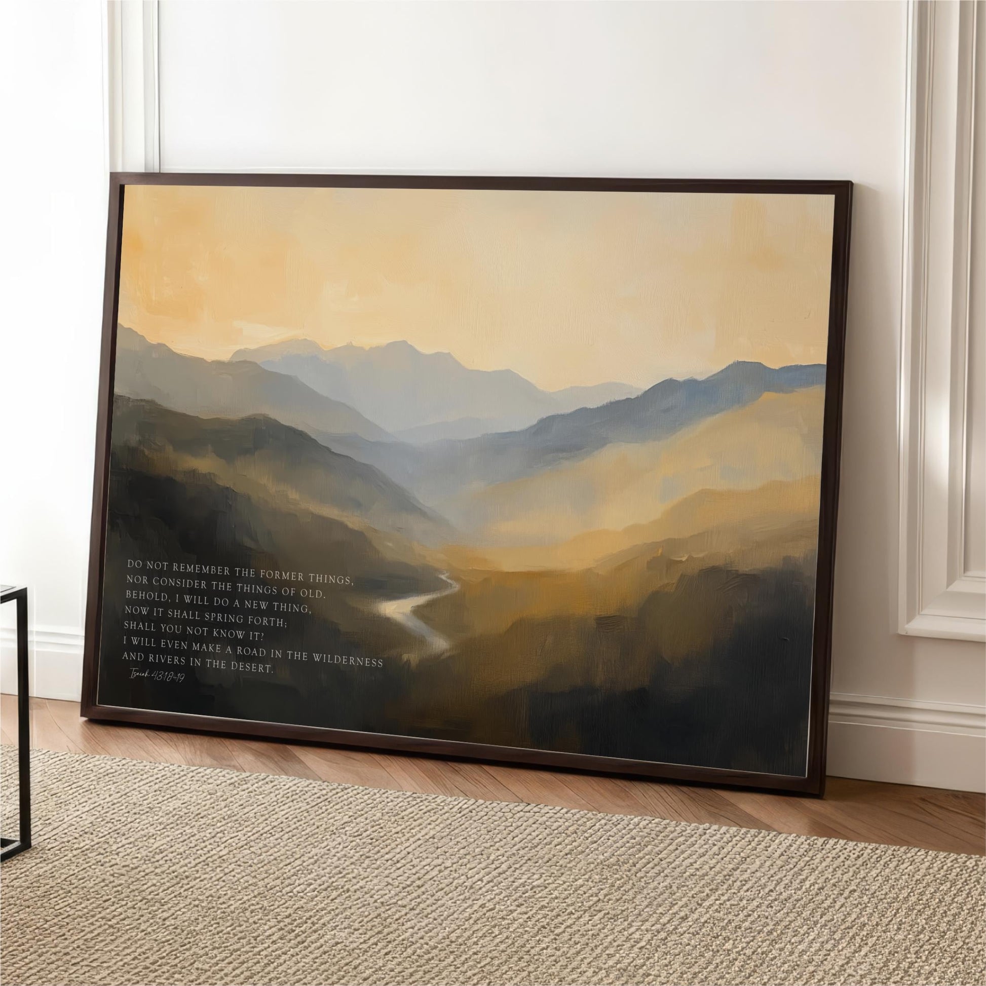 a framed painting of a mountainous landscape with a river winding through it. The painting is displayed on a white wall, and there is a quote in black text below the painting.