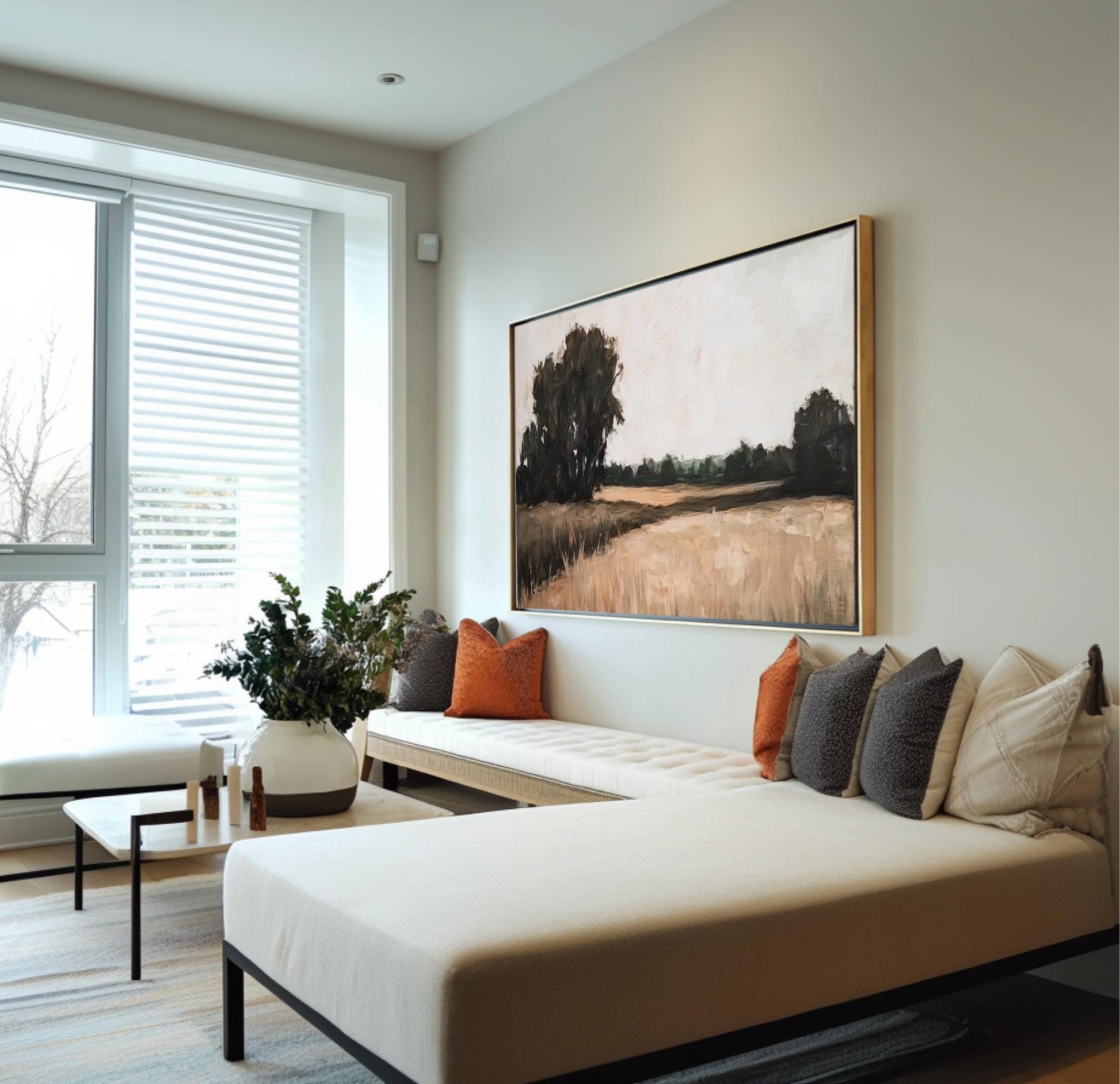a modern living room with a large window, a white sofa with orange and gray throw pillows, and a large painting of a field hanging on the wall.