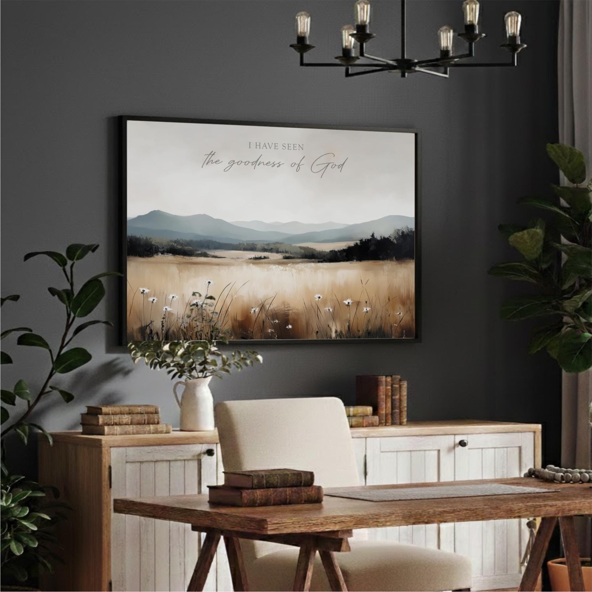 a serene indoor setting with a large framed landscape painting hanging on the wall above a wooden desk. The painting depicts a field with mountains in the background, creating a peaceful and natural atmosphere. The desk is positioned in front of the painting, and there are several books and a vase on the desk, suggesting a workspace or study area.