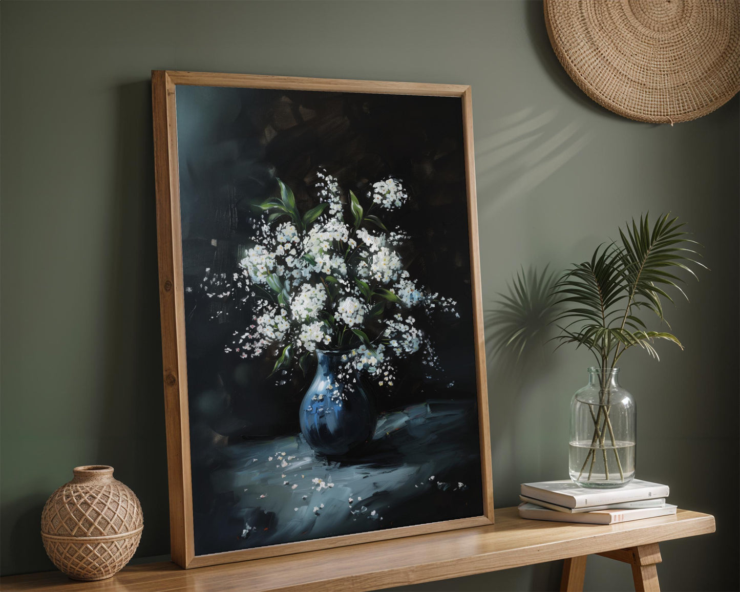 a framed painting of a vase filled with white flowers, placed on a wooden shelf next to a stack of books and a woven basket.