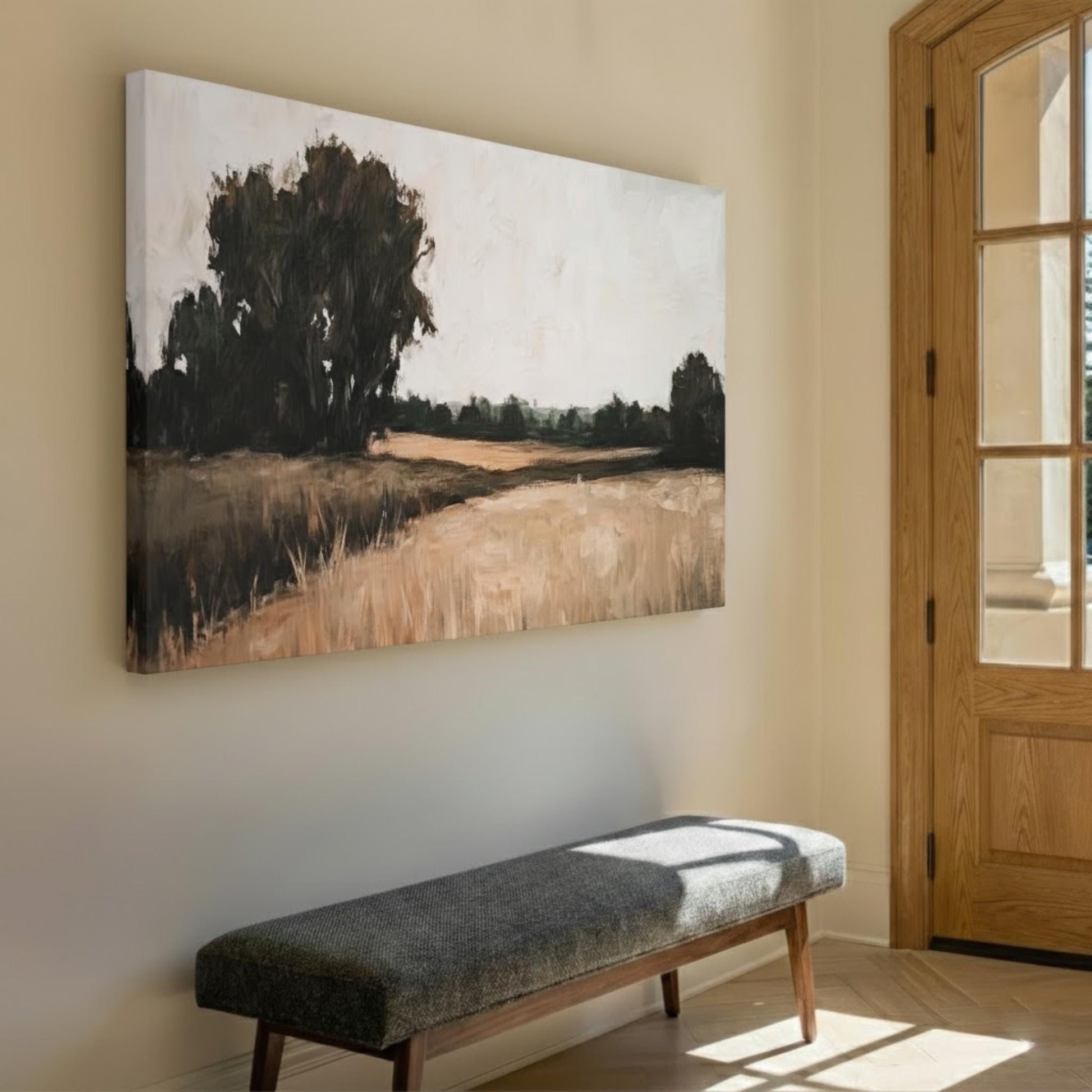 a large painting of a field with trees hanging on a wall, and a gray bench is positioned in front of it.