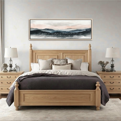 a large wooden bed with a gray comforter and pillows, flanked by two nightstands with lamps. Above the bed is a framed landscape painting depicting a mountain range with a cloudy sky.