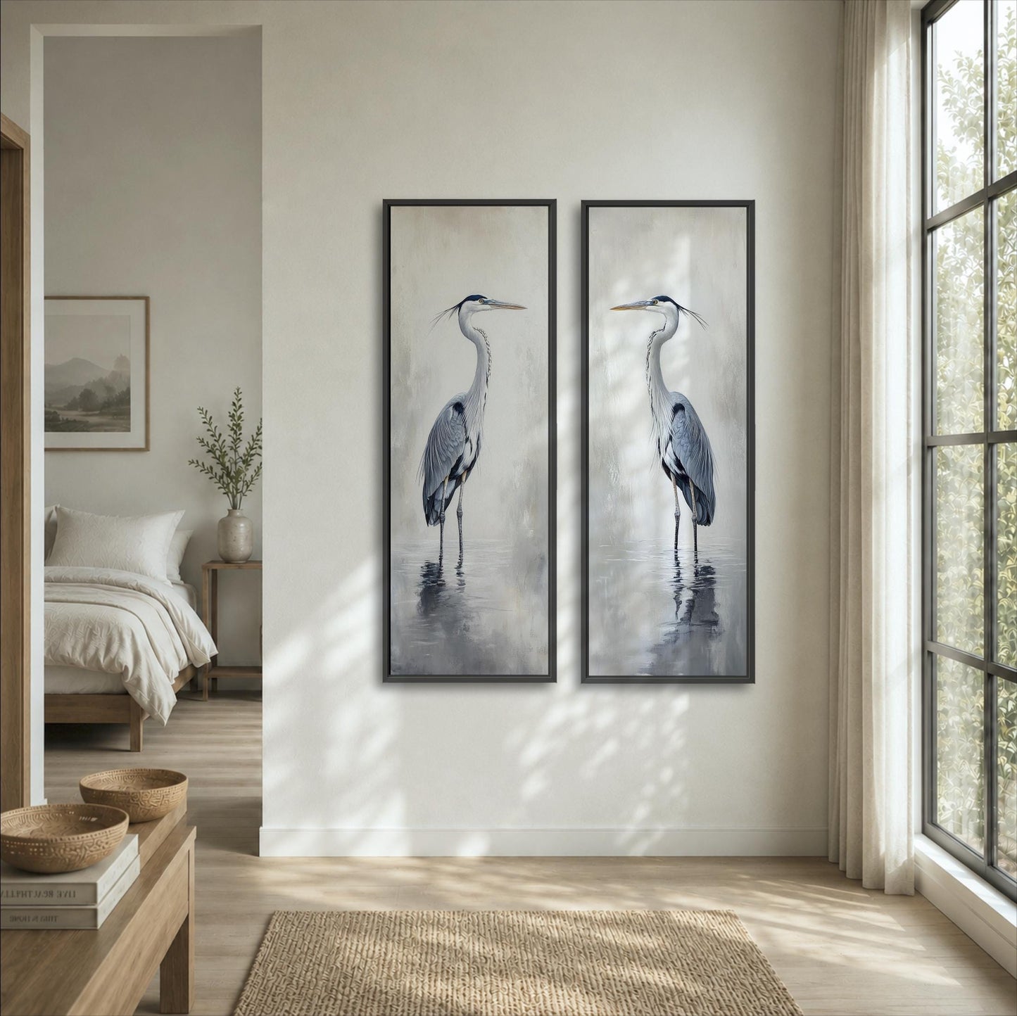 two framed paintings of a tall bird, likely a crane, hanging on a wall in a room with a large window and a bed visible in the background.