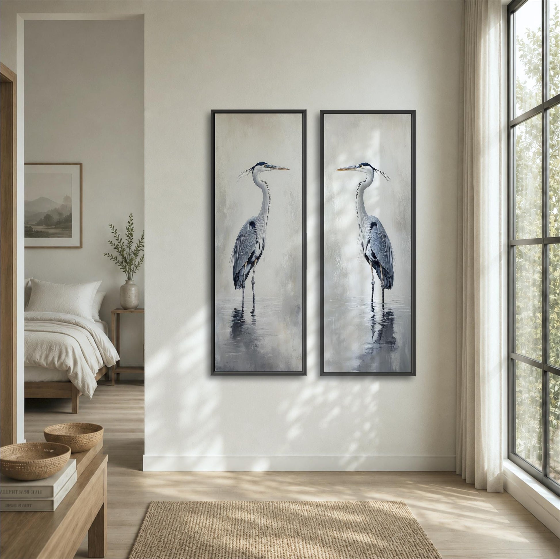 two framed paintings of a tall bird, likely a crane, hanging on a wall in a room with a large window and a bed visible in the background.
