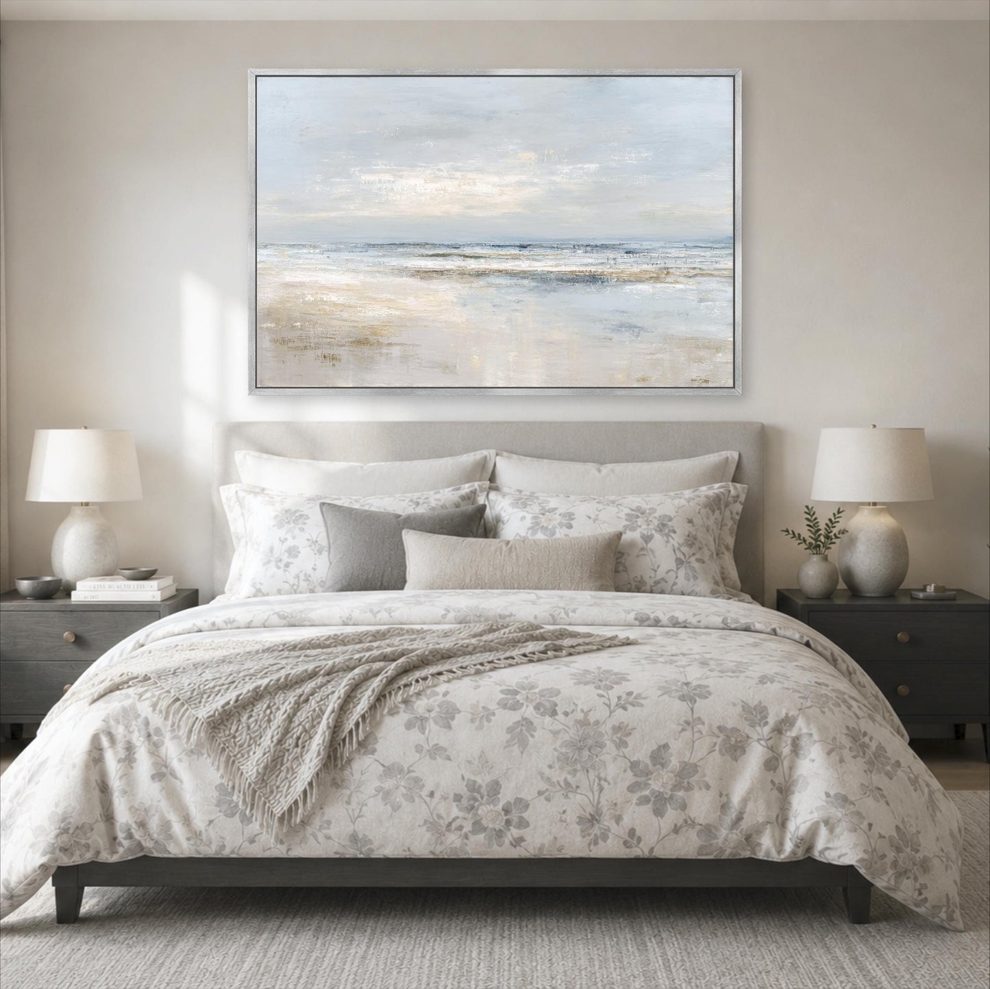 a serene bedroom scene with a large bed adorned with a floral comforter and pillows, flanked by two nightstands with lamps. Above the bed, a large painting of a beach landscape is displayed on the wall, creating a calming and relaxing atmosphere.