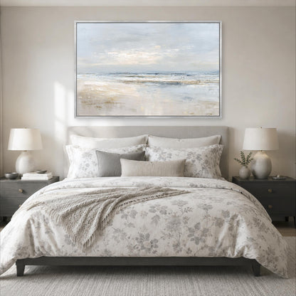 a serene bedroom scene with a large bed adorned with a floral comforter and pillows, flanked by two nightstands with lamps. Above the bed, a large painting of a beach landscape is displayed on the wall, creating a calming and relaxing atmosphere.
