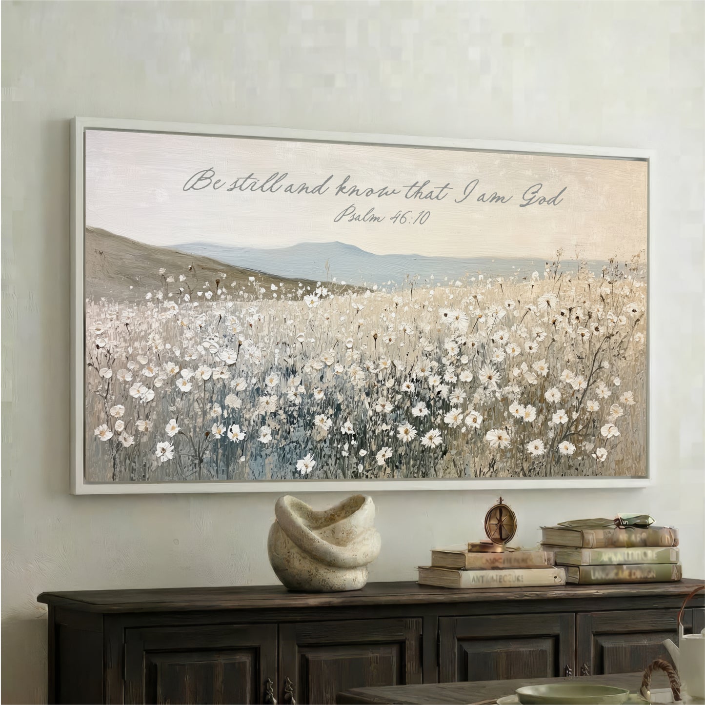 a large framed painting of a field of white flowers hanging on a wall above a wooden cabinet.
