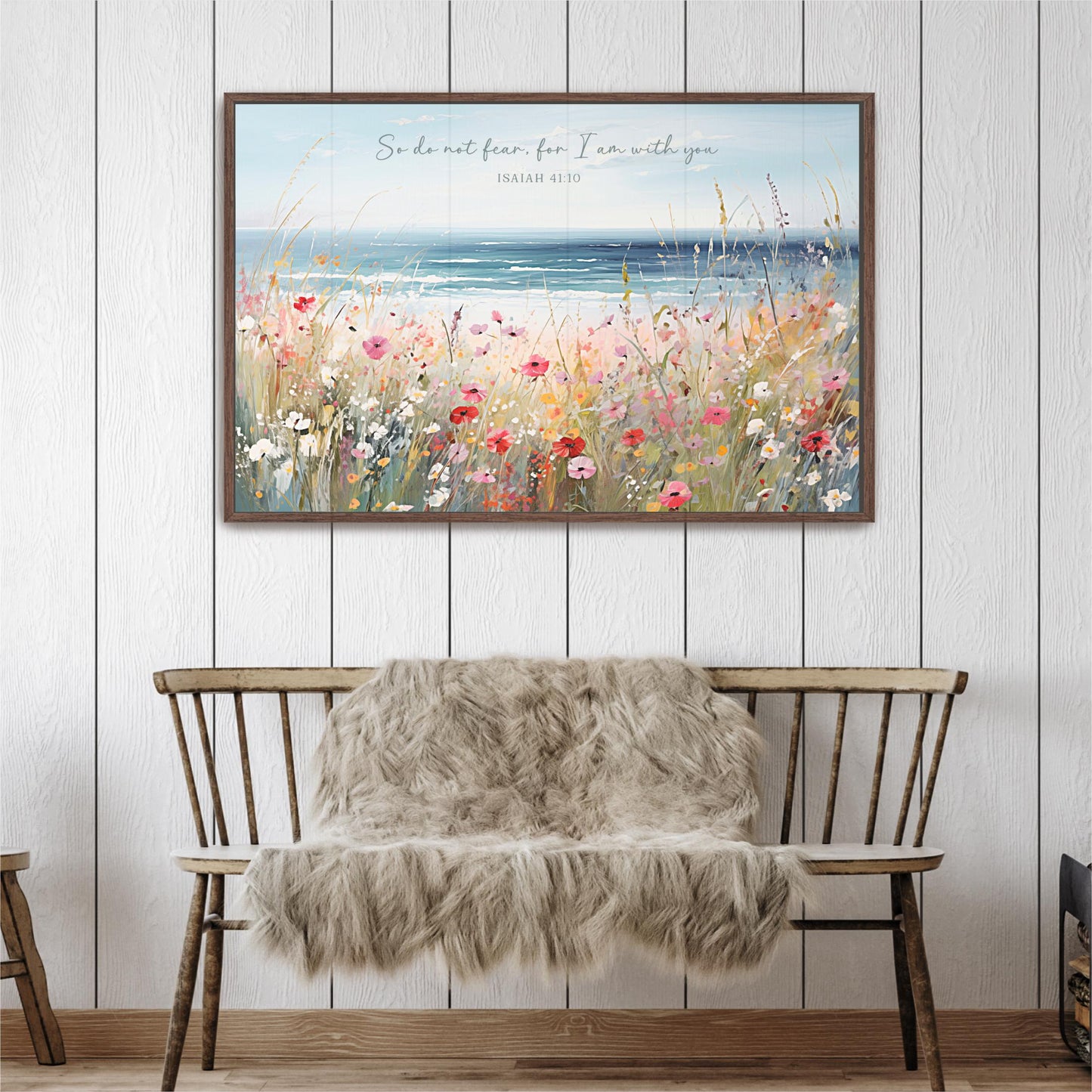 a wooden bench with a furry blanket draped over it, set against a white wall with a framed painting of a field of flowers above it.
