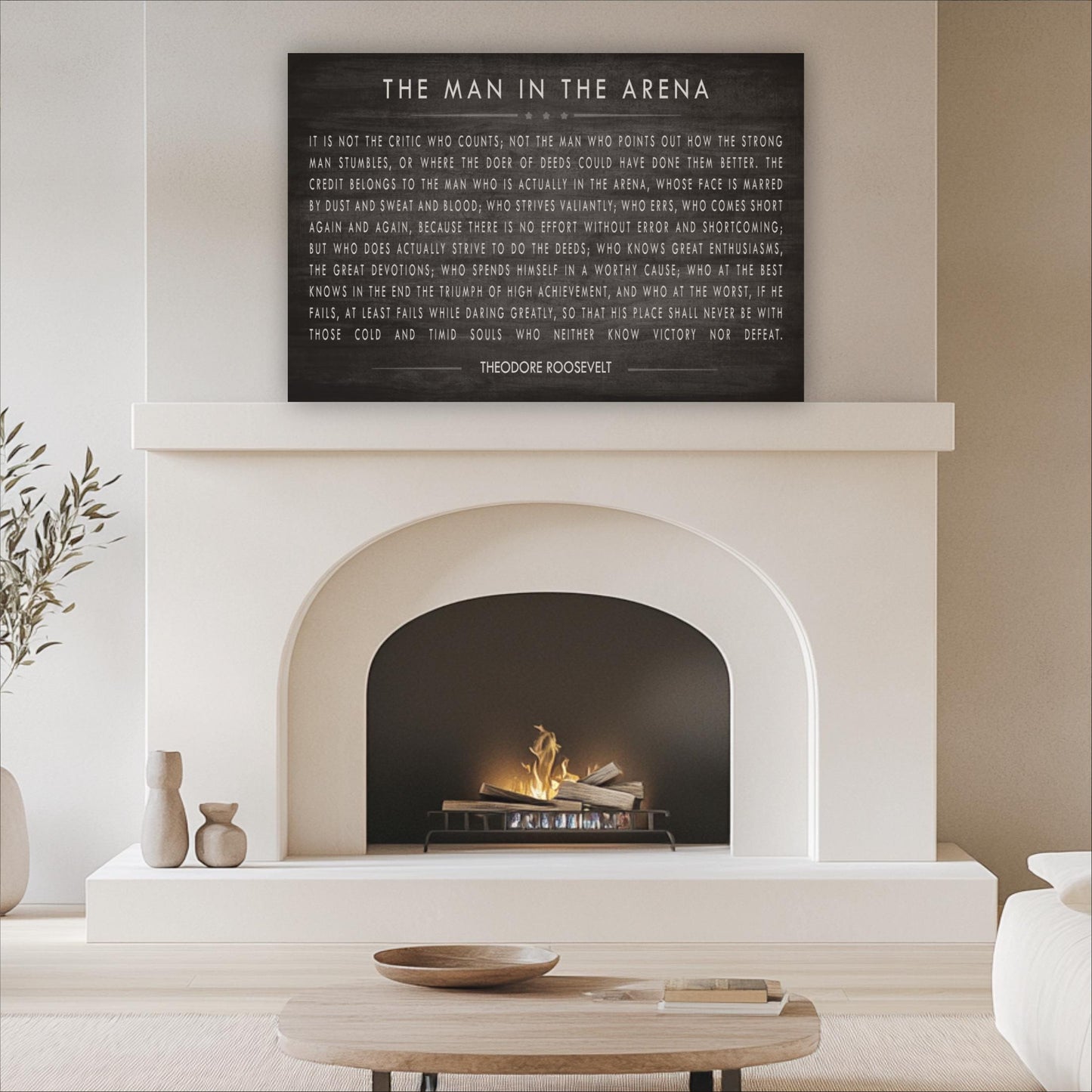 a living room with a fireplace, a wooden coffee table, and a potted plant. Above the fireplace, there is a black framed quote by Theodore Roosevelt.
