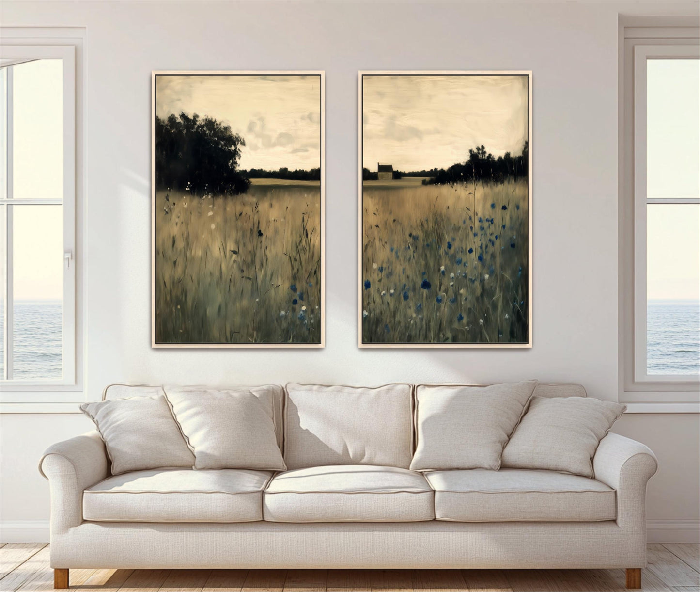 a living room with a white sofa and two framed landscape paintings hanging on the wall above it. The paintings depict a serene countryside scene with a field of tall grass and trees in the background.