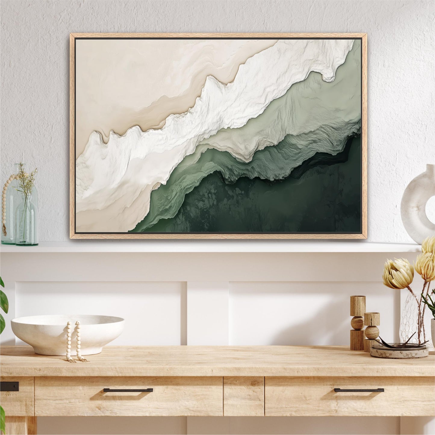 a large abstract painting hanging on a wall above a wooden table with drawers. The painting has a mix of green and white colors, creating a serene and calming atmosphere. The table also has a white bowl and a vase with flowers, adding a touch of elegance to the scene.