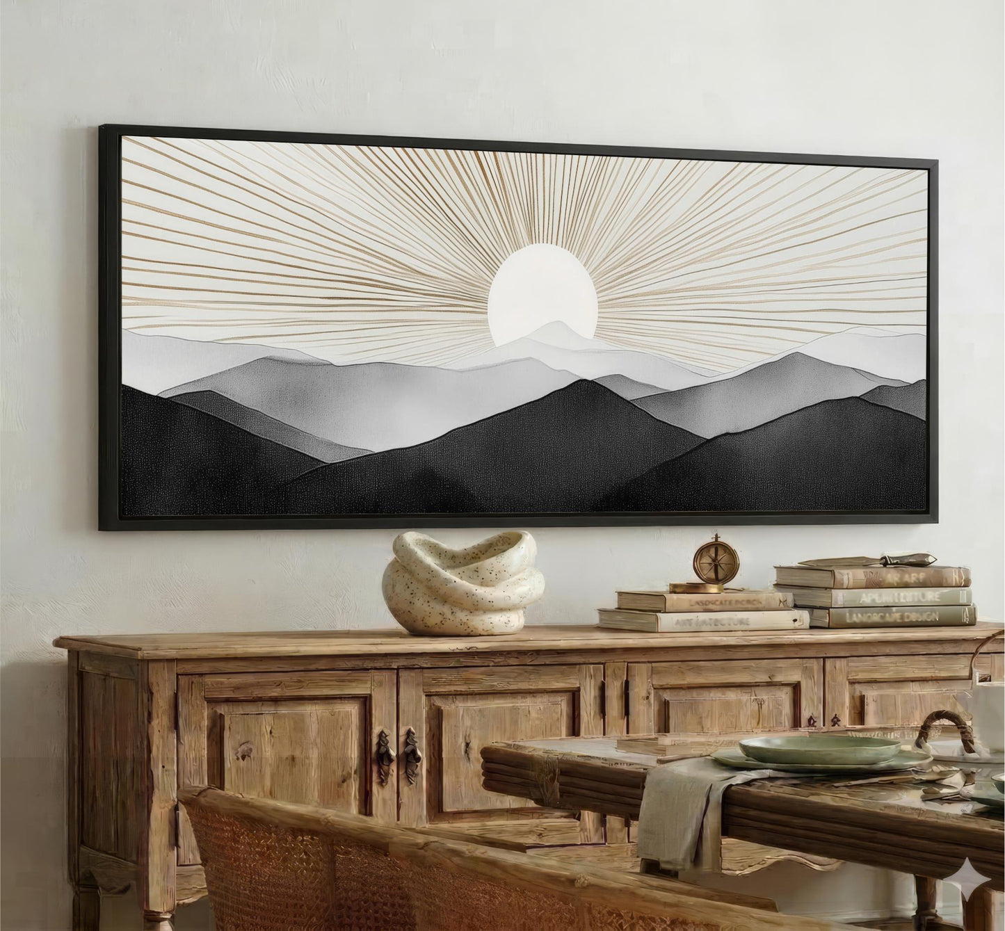 a large black and white landscape painting hanging on a wall above a wooden cabinet. The painting depicts a serene mountain scene with a sun rising over the horizon.