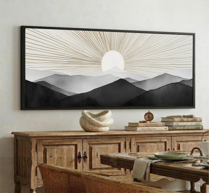 a large black and white landscape painting hanging on a wall above a wooden cabinet. The painting depicts a serene mountain scene with a sun rising over the horizon.
