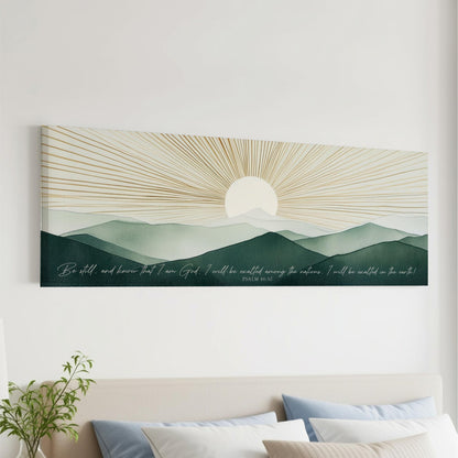 a large canvas print depicting a serene landscape with mountains and a sun rising over the horizon. The text overlay on the canvas reads "Be still, and know that I am God. I will be victorious over the nations. I will be victorious on earth!"