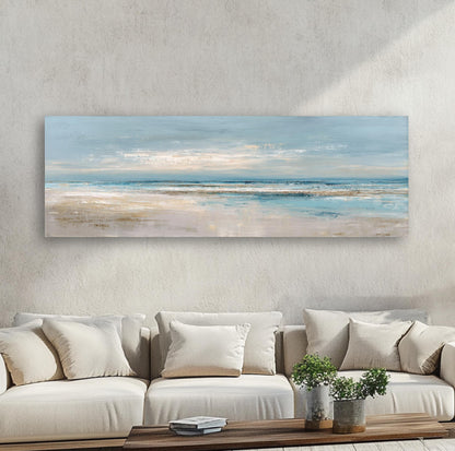 a large, rectangular painting of a beach scene hanging on a wall above a beige sofa with white pillows.
