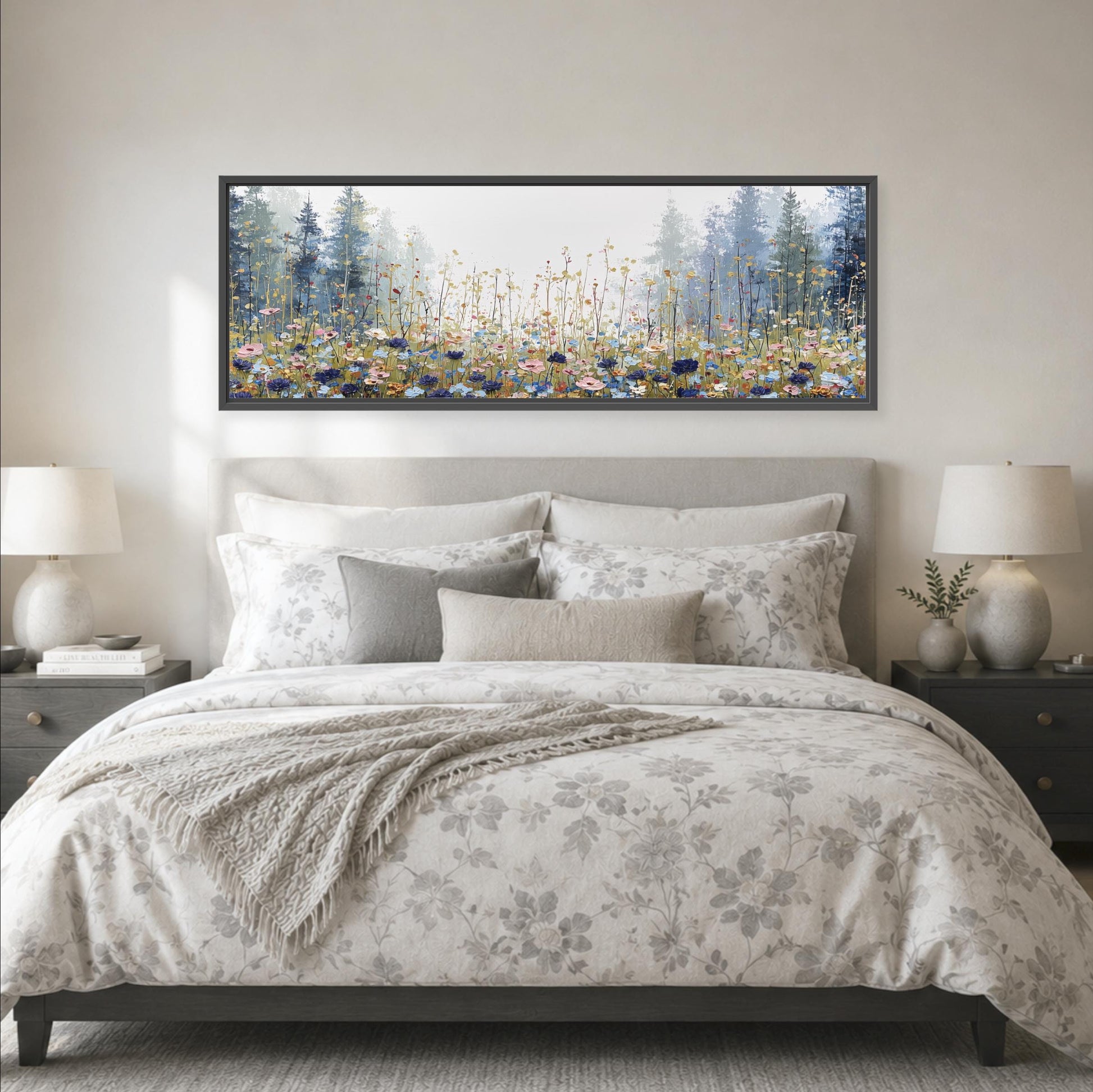 a large bed with a floral comforter and pillows, flanked by two nightstands with lamps. Above the bed is a large framed painting depicting a forest scene with tall trees and a field of flowers.