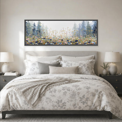 a large bed with a floral comforter and pillows, flanked by two nightstands with lamps. Above the bed is a large framed painting depicting a forest scene with tall trees and a field of flowers.