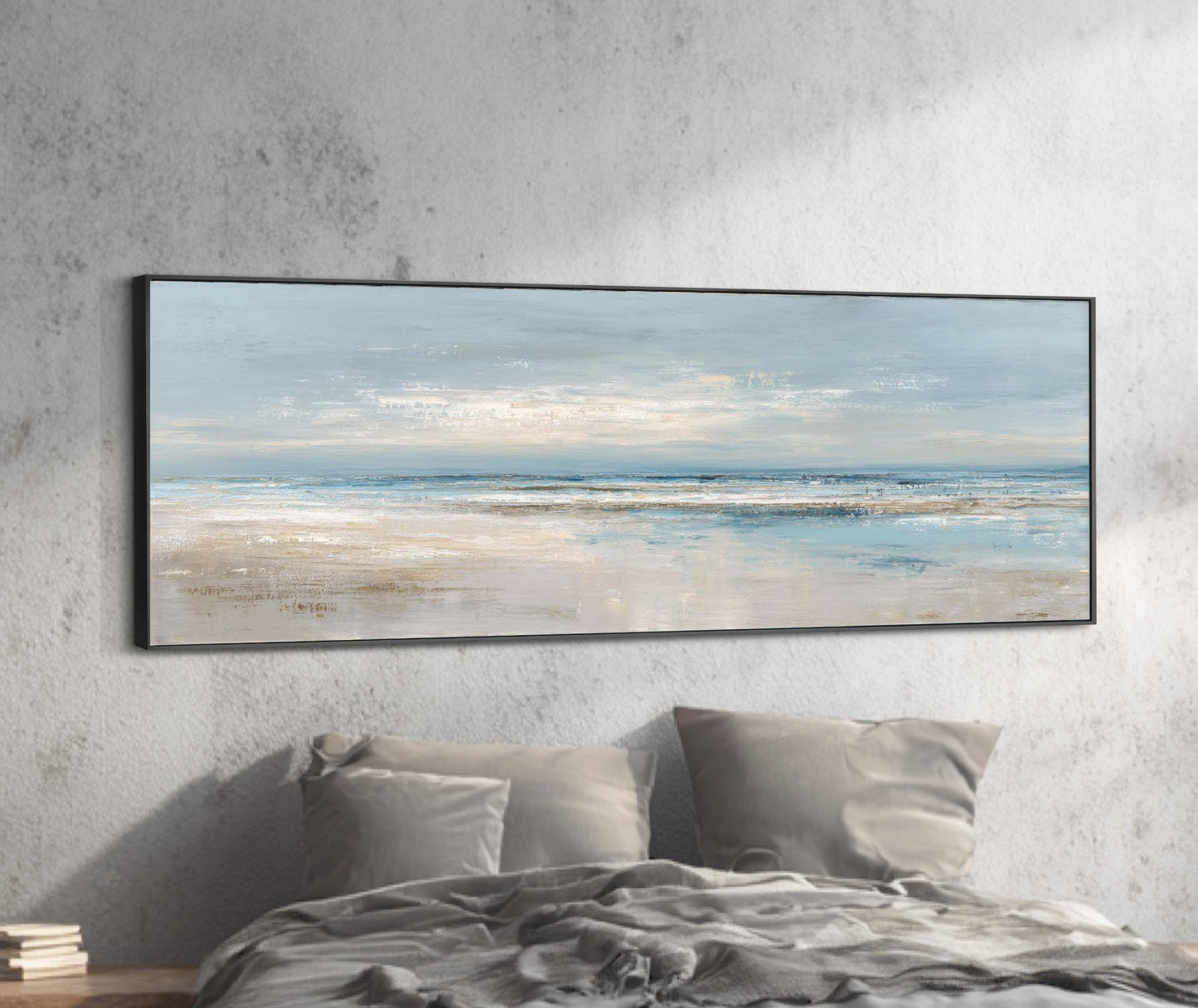 a large, framed painting of a serene beach scene hanging on a wall above a bed with gray pillows.