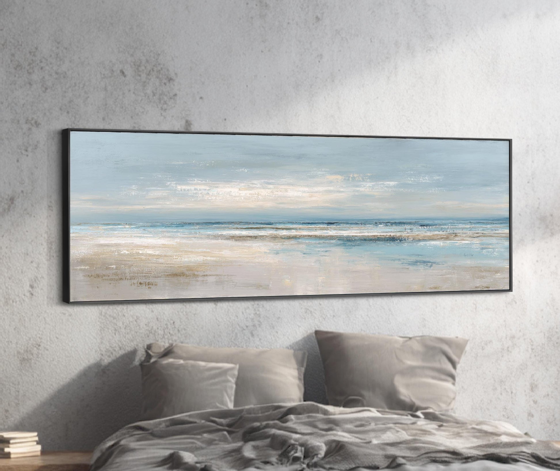 a large, framed painting of a serene beach scene hanging on a wall above a bed with gray pillows.