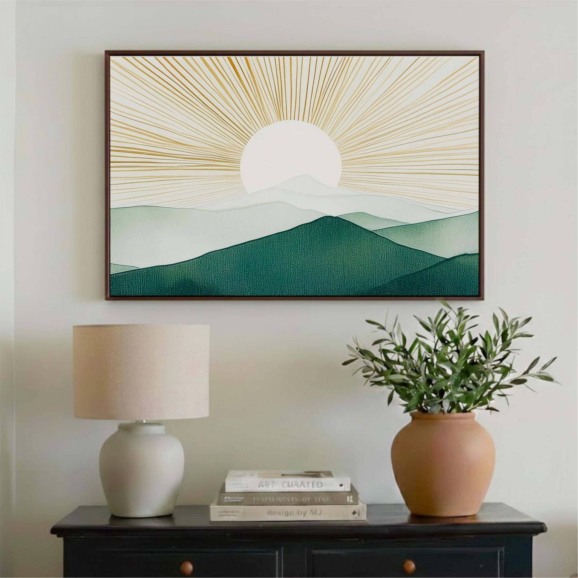 a framed artwork depicting a serene landscape with a sun rising over a mountain range, accompanied by a potted plant and a lamp on a black dresser.