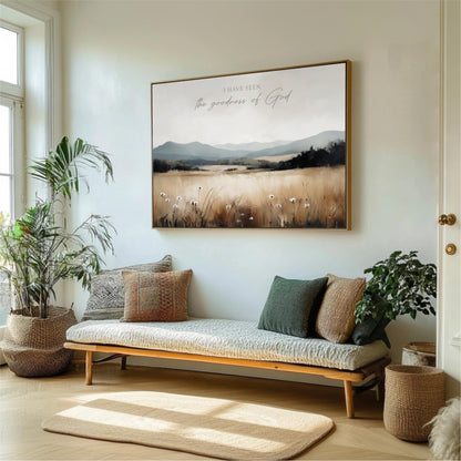 a living room with a large framed landscape painting hanging on the wall above a wooden bench with pillows. The painting depicts a serene countryside scene with mountains and a field of flowers. The room is decorated with potted plants and a rug, creating a cozy and inviting atmosphere.