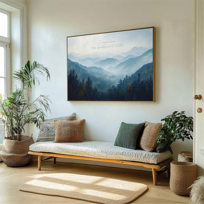 a living room with a large framed picture of a mountain landscape hanging on the wall above a couch with pillows. The room is decorated with potted plants and a rug, creating a cozy and inviting atmosphere.
