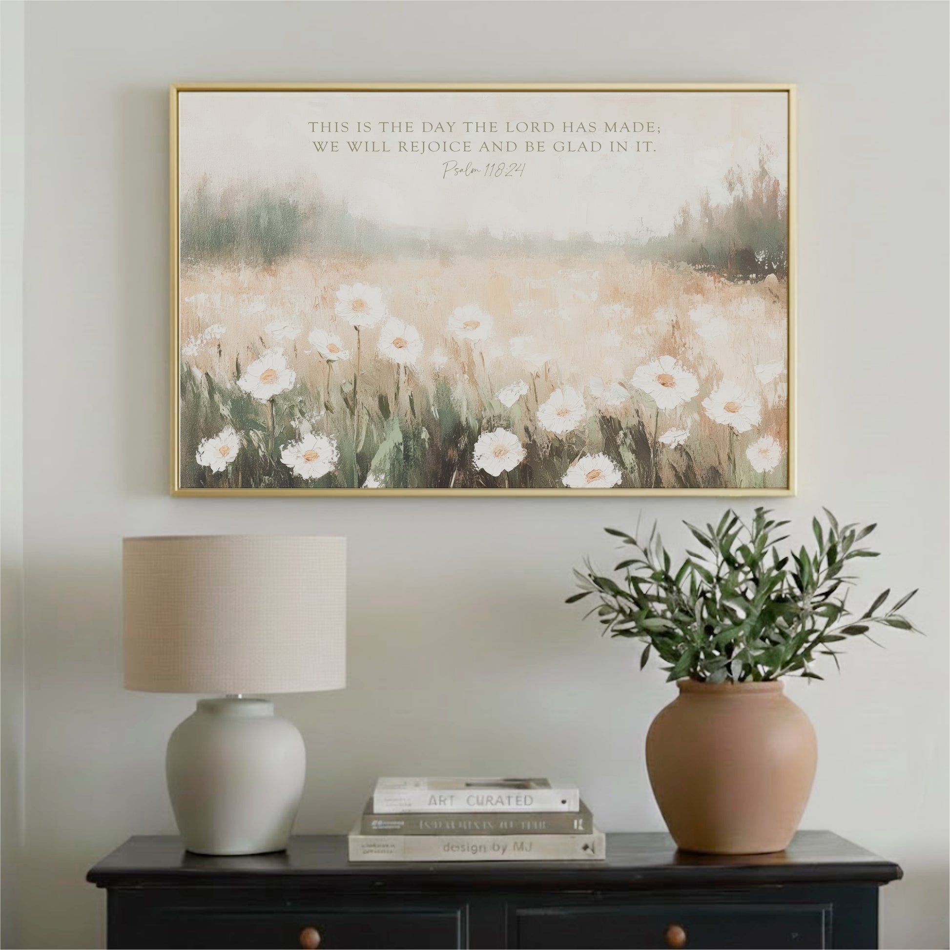a wall-mounted painting of a field of white flowers, a lamp, a potted plant, and a stack of books on a black dresser.