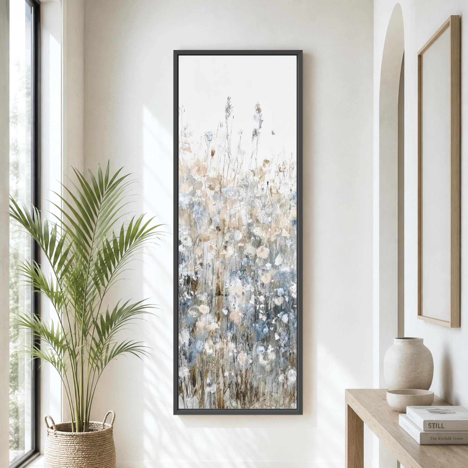 a large painting of flowers hanging on a wall, with a potted plant to the left and a wooden table with a vase to the right.