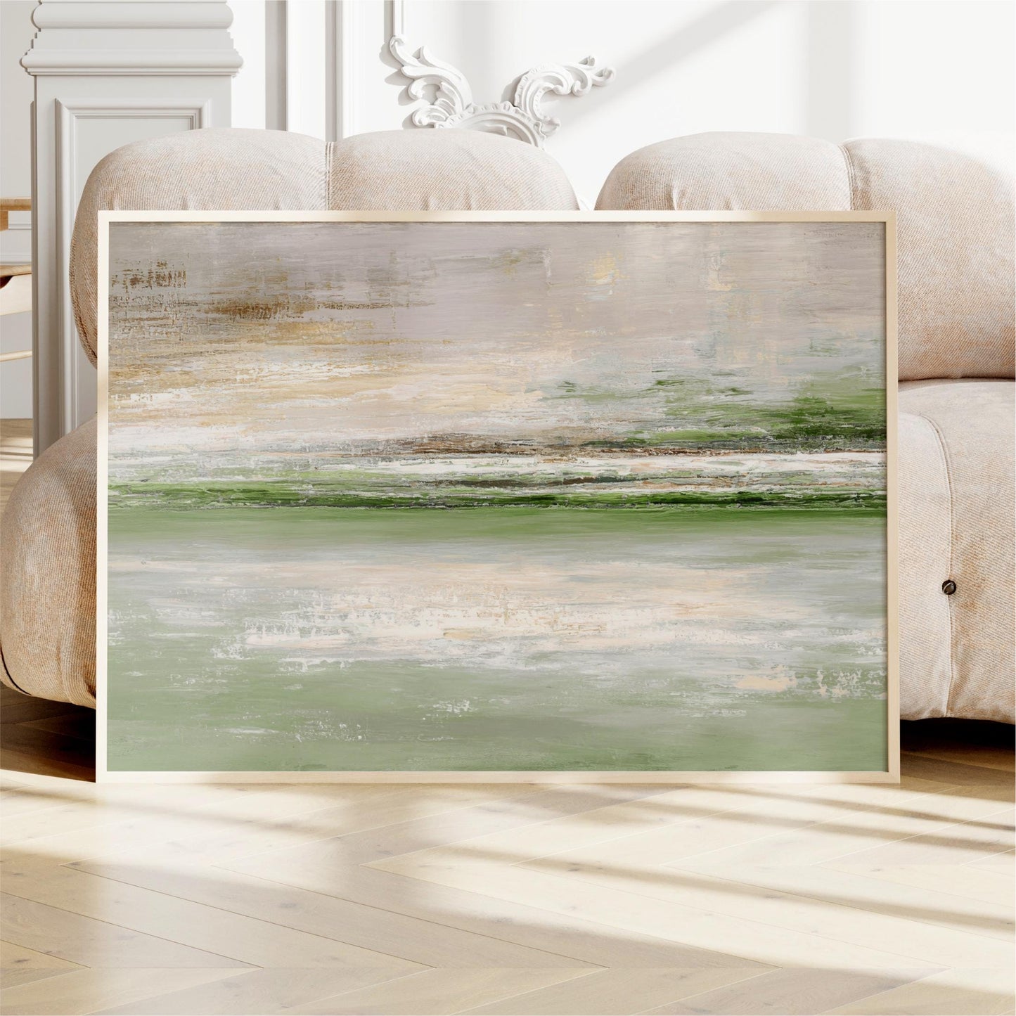 a large abstract painting displayed on a wooden floor in front of a beige sofa.