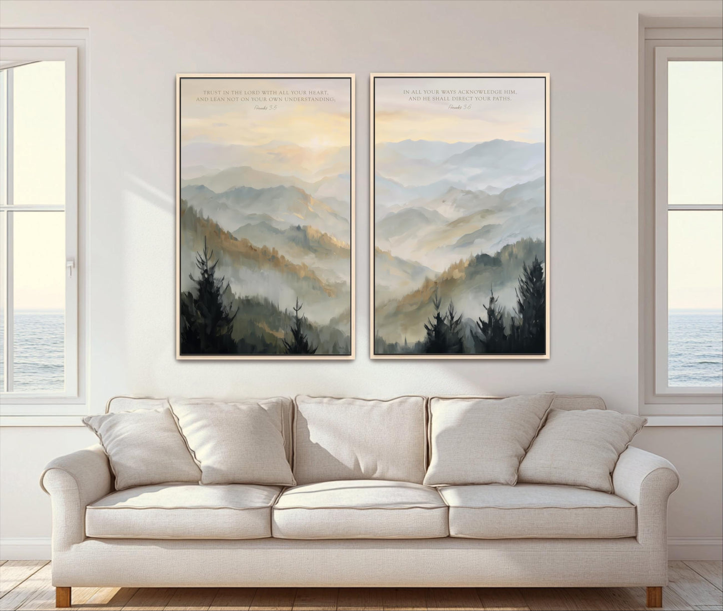 a serene living room with a white sofa and two framed landscape paintings hanging on the wall above it. The paintings depict a tranquil mountain scene with trees and a hazy, golden sky.