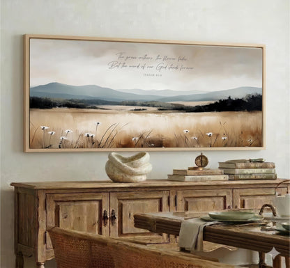 a large framed painting of a serene landscape with mountains, a field of flowers, and a text overlay that reads "The grass without the flower stands dead But the word of our God stands forever".