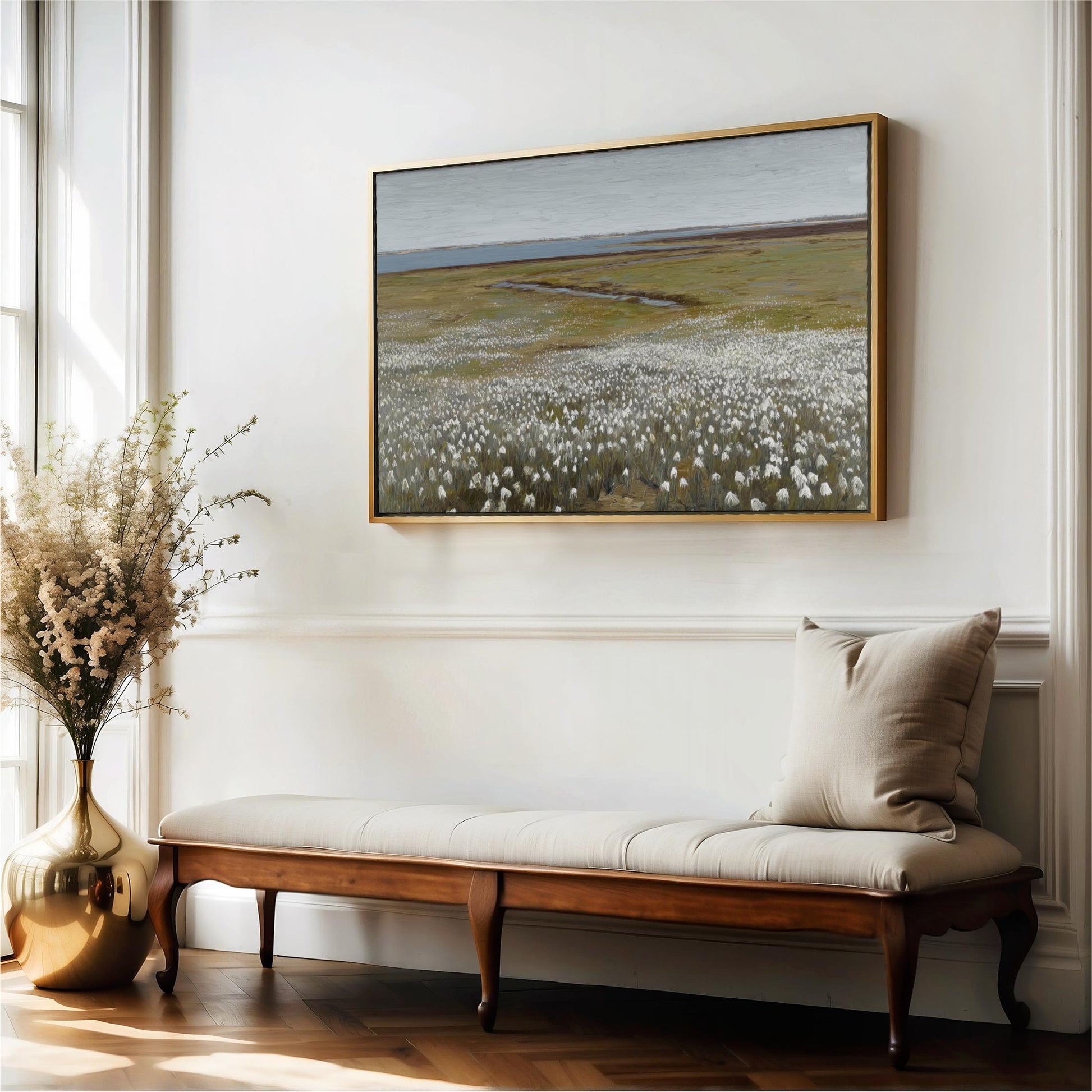 a large painting of a field with white flowers hanging on a white wall above a wooden bench with a beige cushion.