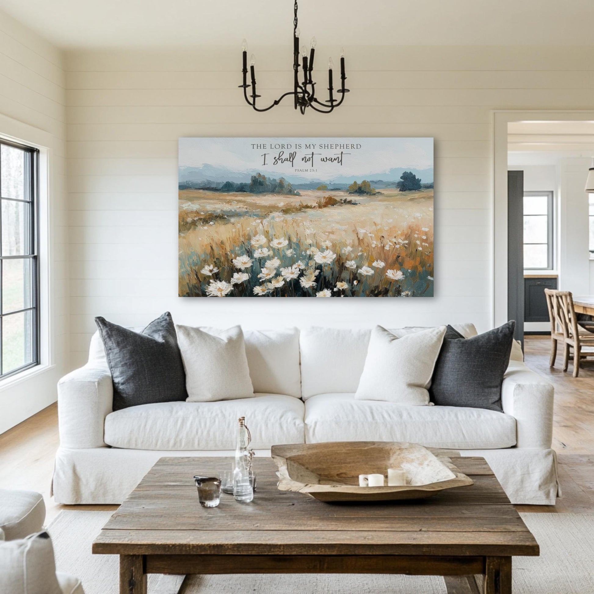 a living room with a large painting of a field of flowers hanging on the wall above a white sofa. The painting is titled "The Lord is my shepherd" and depicts a pastoral landscape with a chandelier hanging from the ceiling.