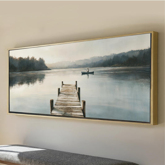 Bring a sense of peace and quiet into your home with this panoramic horizontal lake landscape featuring a weathered dock stretching into calm waters and a lone fisherman drifting by in a canoe beneath the soft morning light. The muted palette of warm creams, soft blues, taupe, and deep forest greens creates a calming focal point that complements modern organic, rustic, Scandinavian, and lake house interiors. Whether displayed above a sofa,