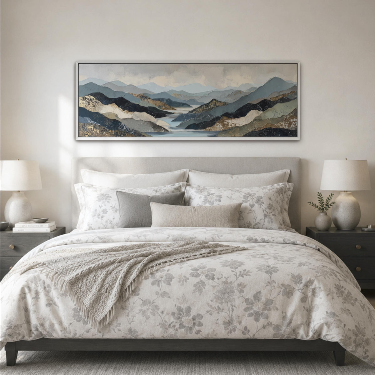 a large bed with a floral bedspread and pillows, flanked by two nightstands with lamps. Above the bed is a large framed landscape painting depicting a mountainous, forested scene.