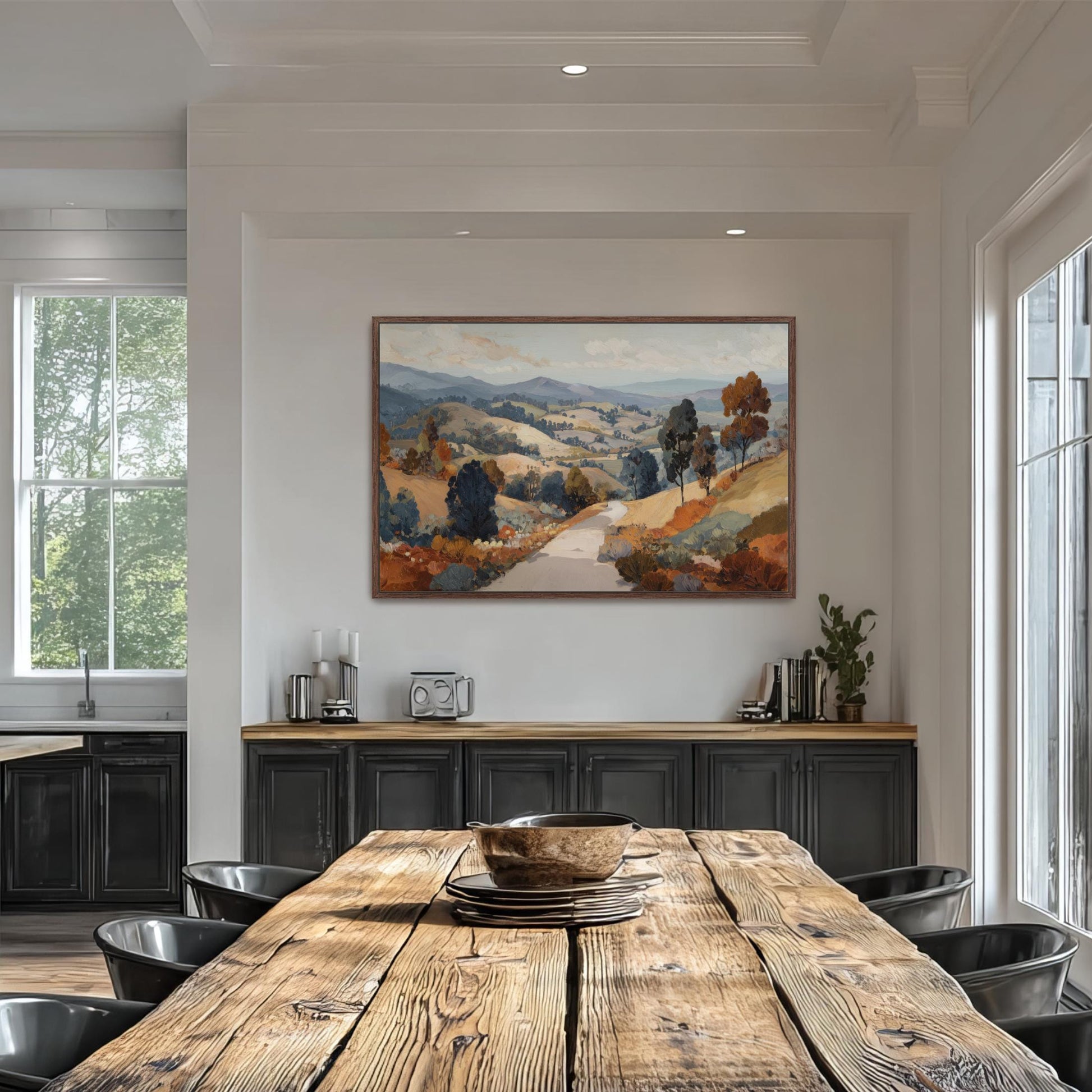 a large, colorful landscape painting hanging on a white wall above a wooden dining table. The table is surrounded by black chairs, and there are several books and decorative items on the table.